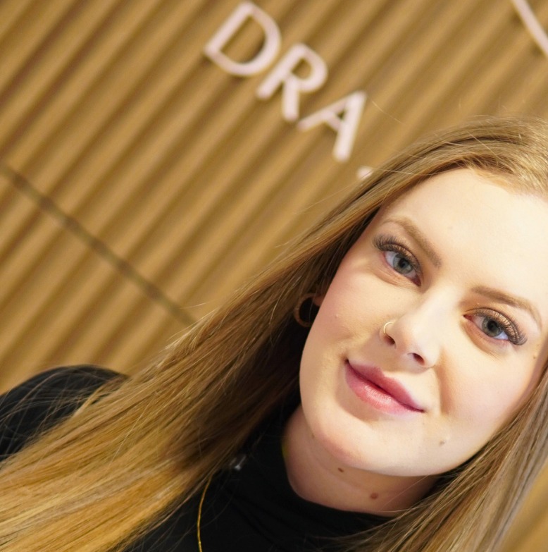 Camila Domanski diante da parede de ripas de madeira da própria clínica, com as letras douradas do nome gravadas ao fundo